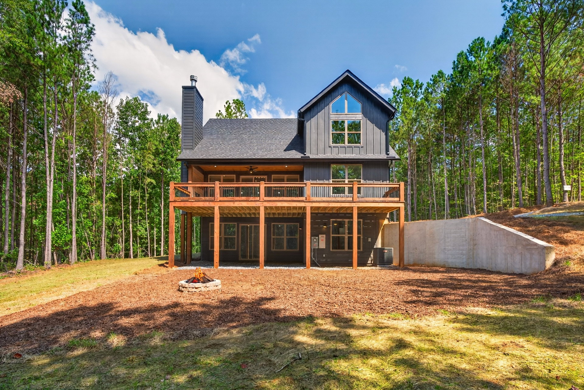 Back of the home with stone chimney, wood deck, and fire pit at 824 Banks Rd, Ellijay, GA