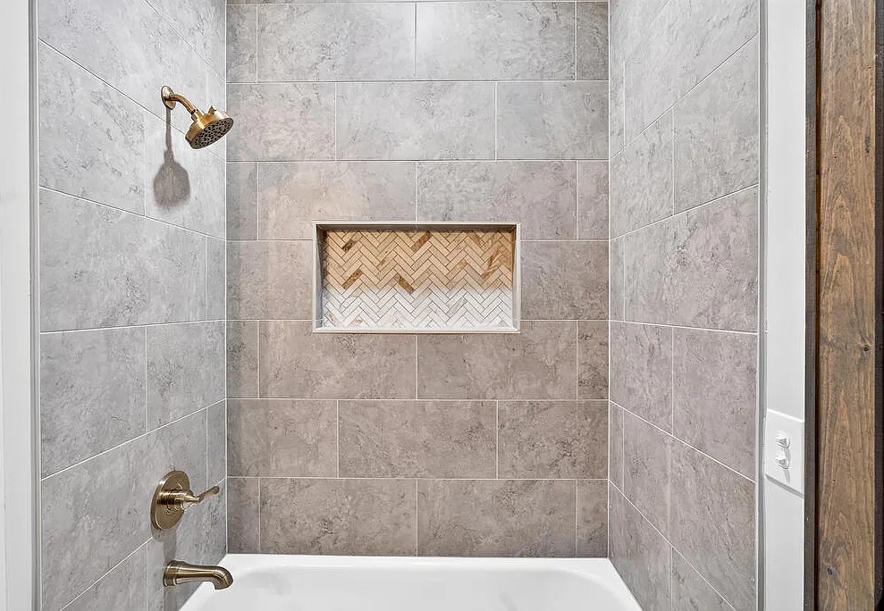 Tiled tub surround with gold fixtures and a herringbone shower niche