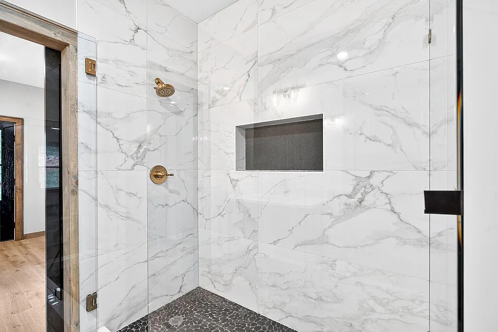 Walk-in shower with marble-look tile, pebble floor, and gold fixtures
