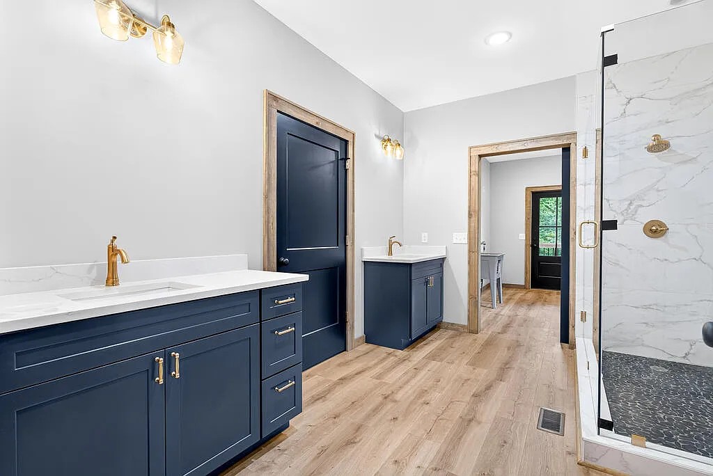 Bath with navy vanities, gold fixtures, and a marble-look walk-in shower