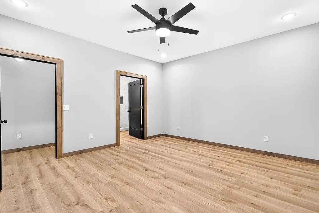 Bedroom with light wood floors, wood-trimmed doors, and a black ceiling fan