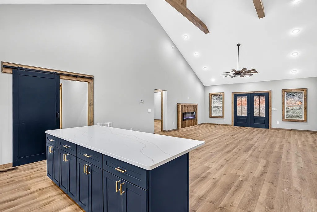 Open living area with a navy kitchen island, vaulted beamed ceiling, and a sliding barn door