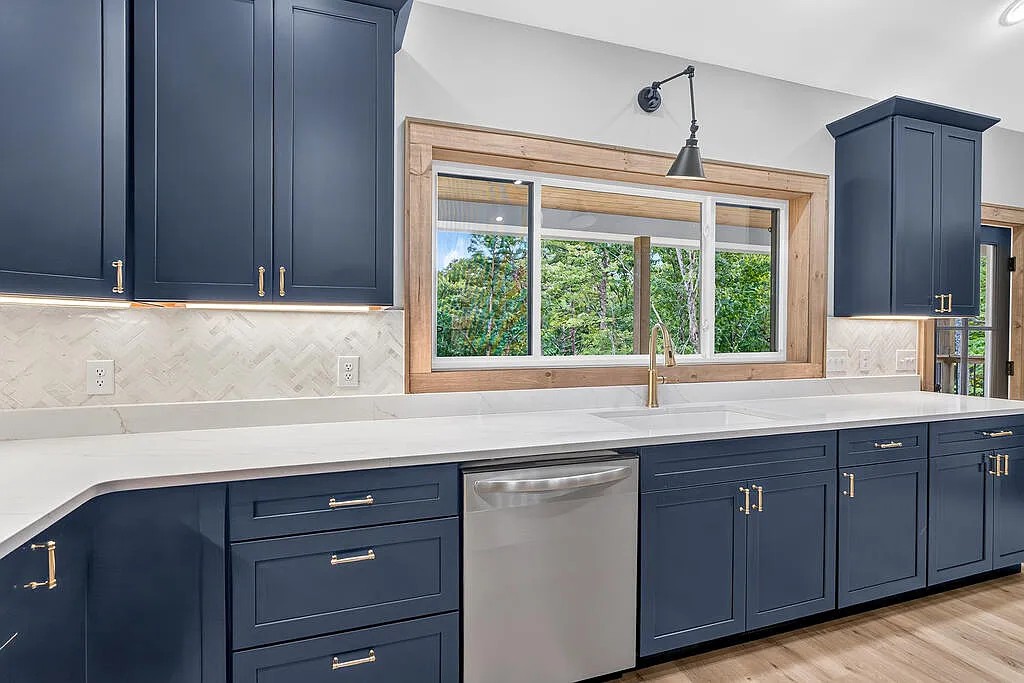 Kitchen sink with navy cabinets, herringbone tile backsplash, and a wood-framed window
