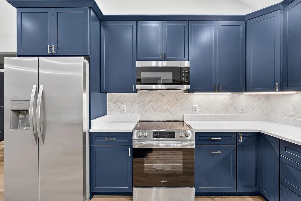 Kitchen with navy shaker cabinets, herringbone tile, and stainless appliances