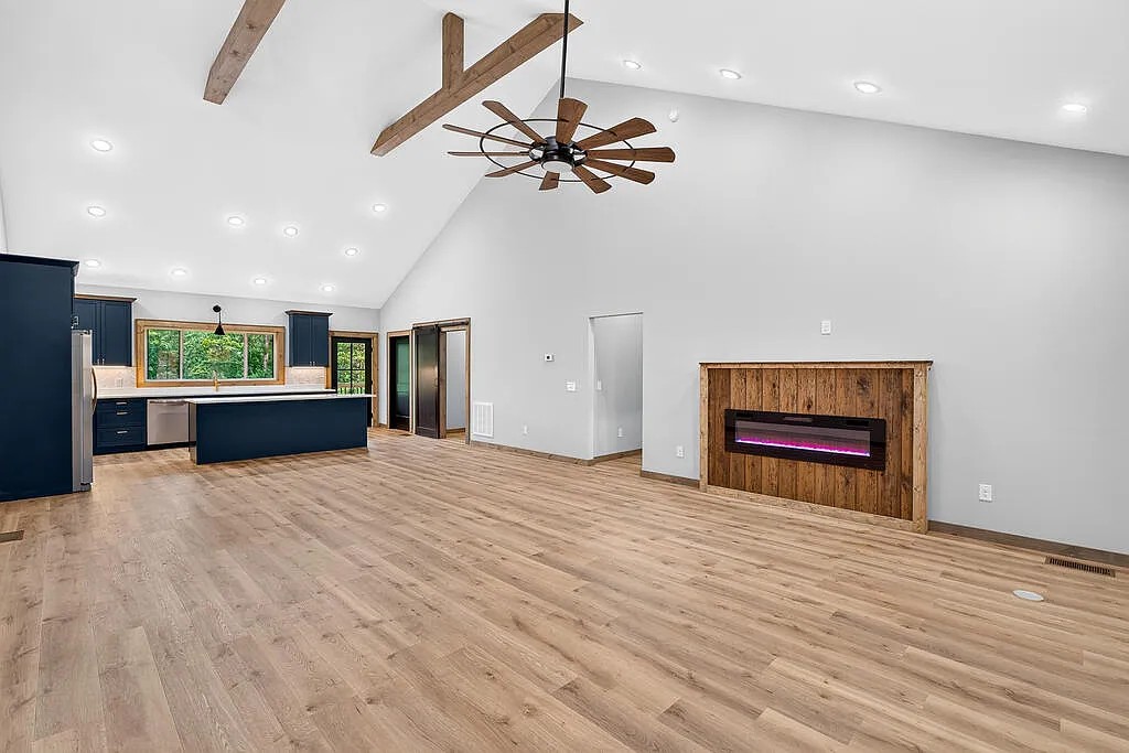 Open kitchen and living area with navy cabinets, vaulted beamed ceiling, and a wood-surround fireplace