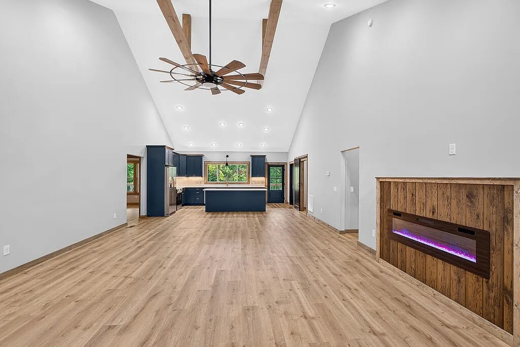 Open kitchen and living area with navy cabinets, vaulted beamed ceiling, and a wood-surround fireplace