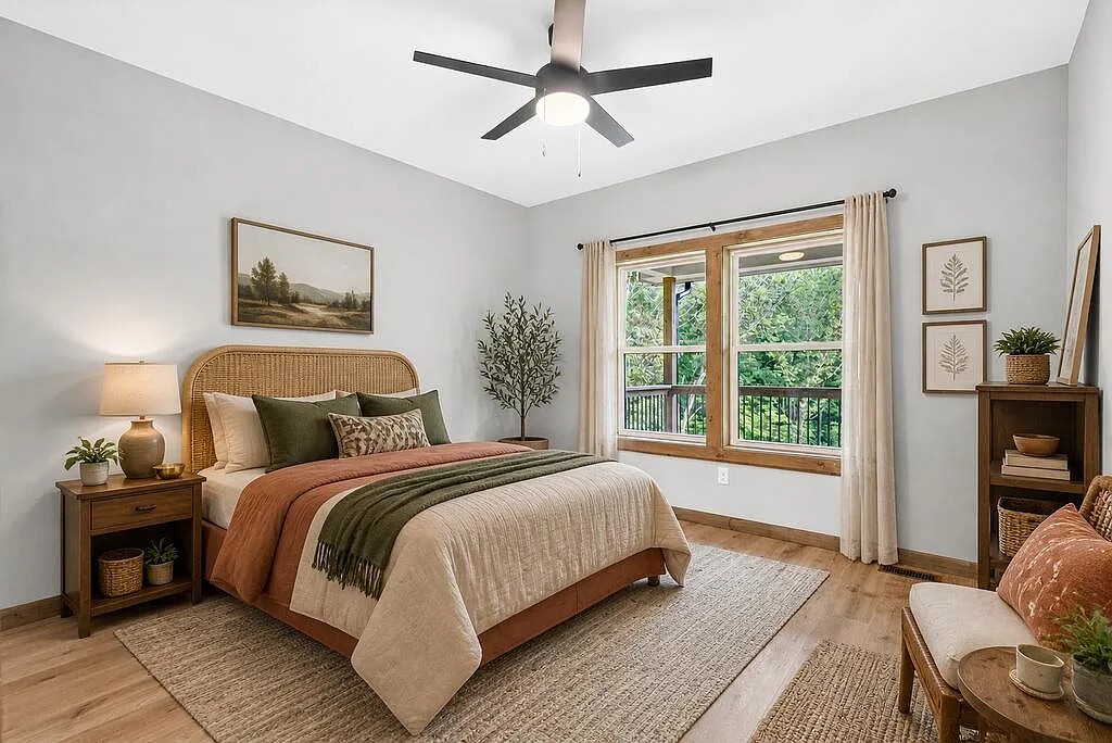Bedroom with a woven headboard, wooded-view windows, and a ceiling fan