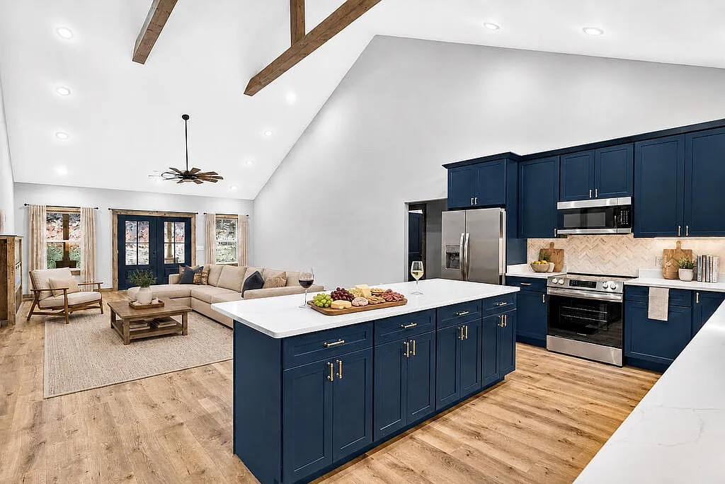 Open kitchen and living area with navy cabinets, vaulted beamed ceiling, and a beige sectional