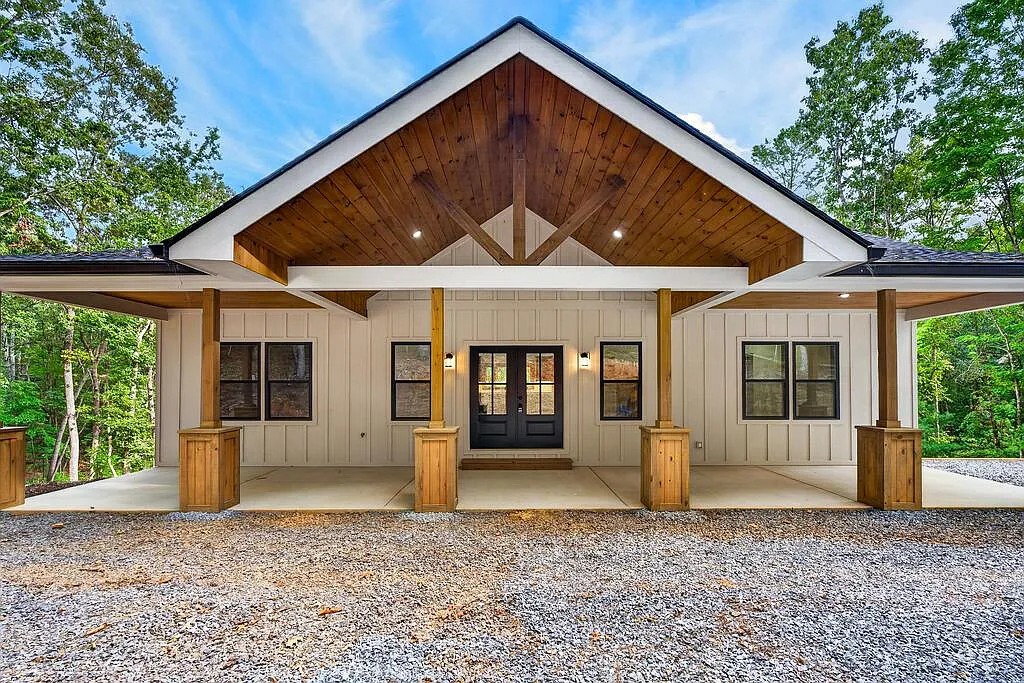 Front exterior of a white board-and-batten home with a timber porch and black-trimmed windows