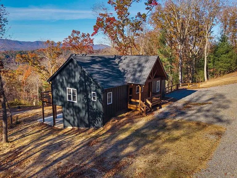 Aerial view of a charcoal gabled home with wood porches among autumn trees