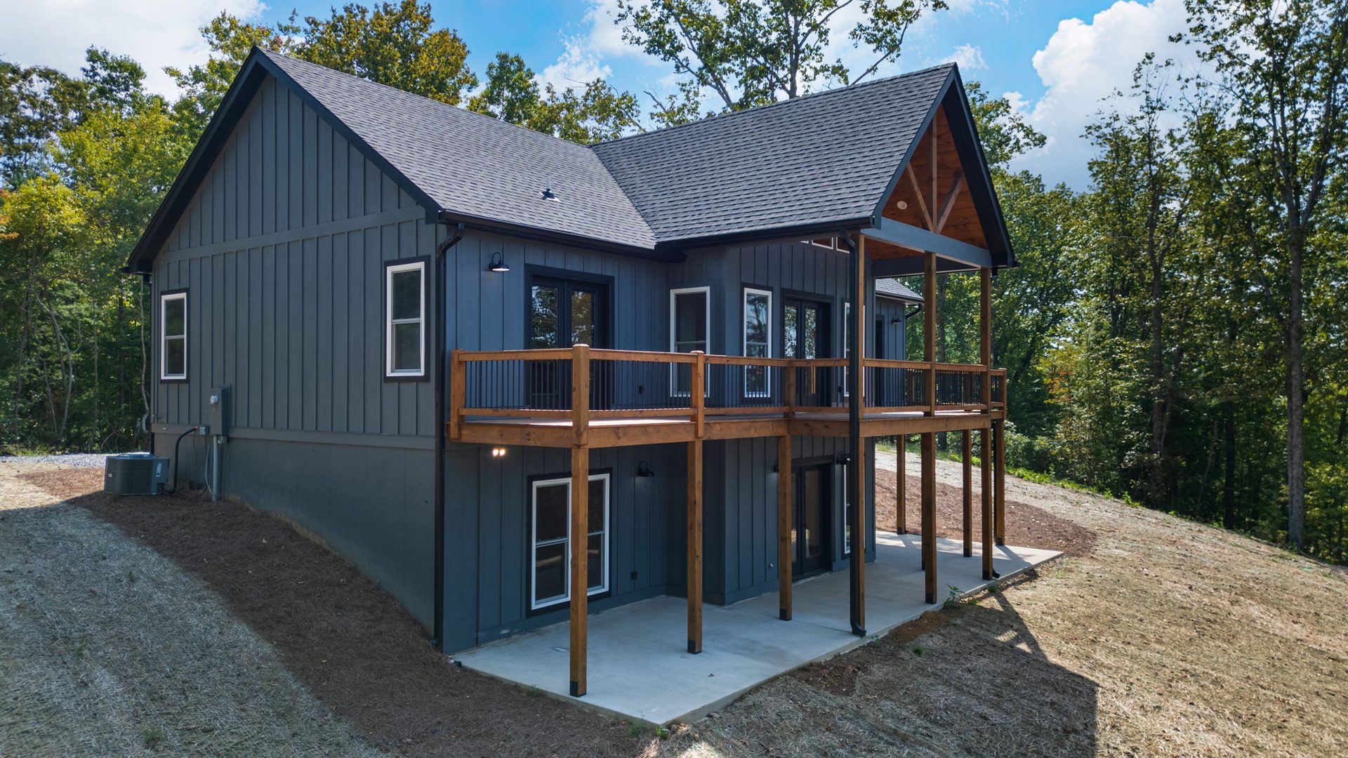 Grey vertical-siding home with two levels of wood porches in a green wooded setting
