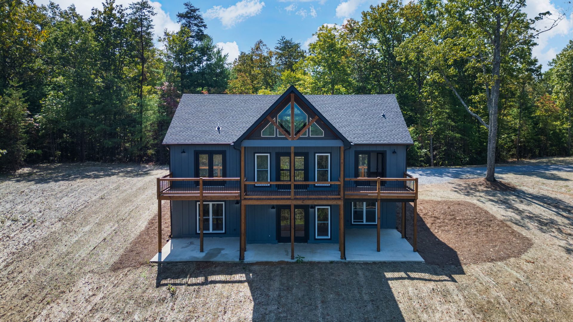 Rear of a grey home showing multi-level wood decks and a large gable window
