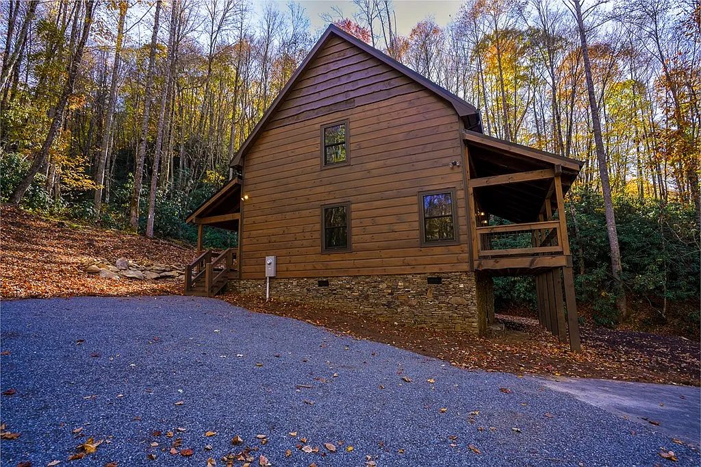 Side of a wood cabin with a stone foundation and gravel drive under fall foliage