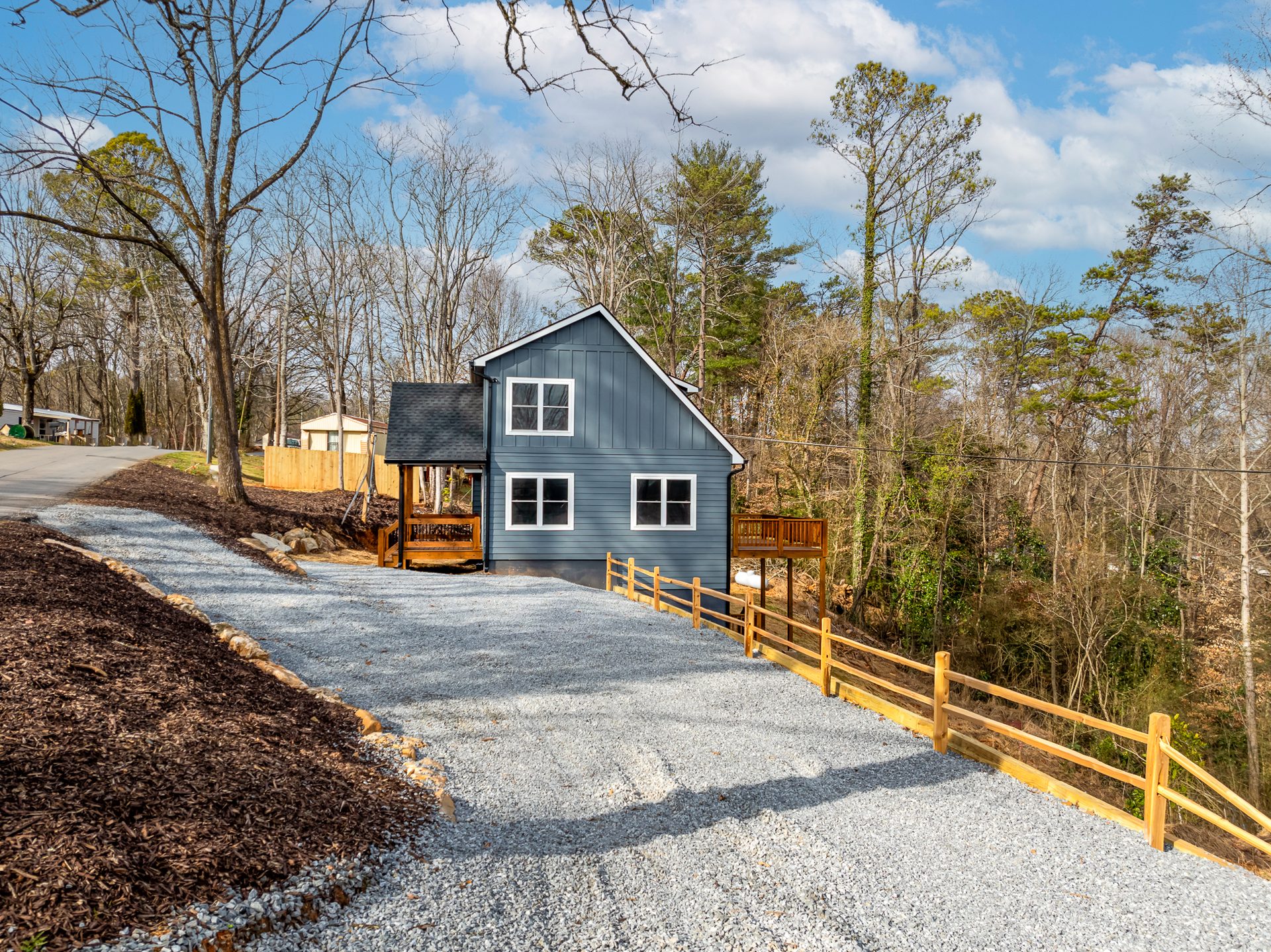 Blue-gray home at the top of a gravel driveway with a wood post-and-rail fence