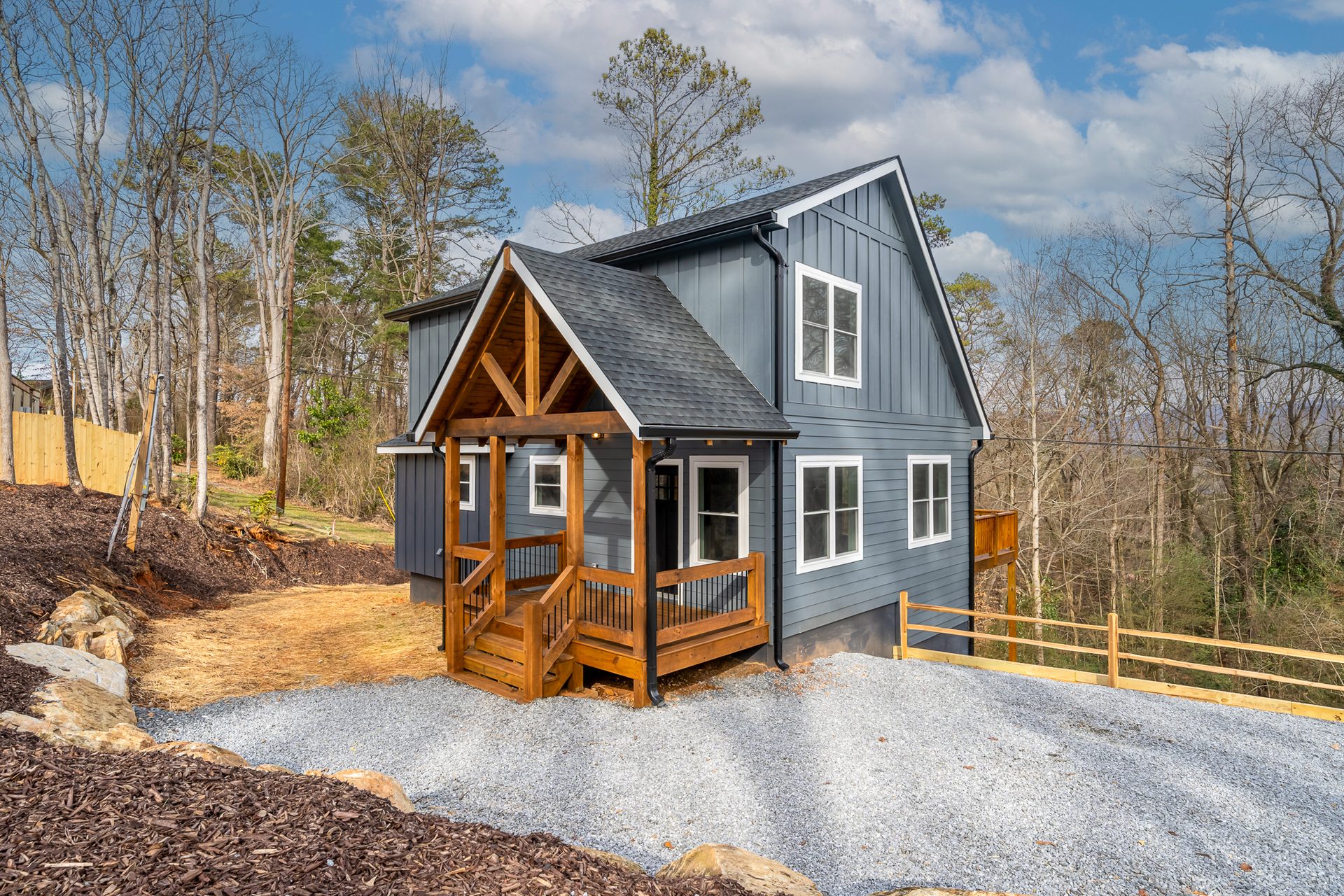 Front of a blue-gray home with white-trimmed windows and a warm timber porch