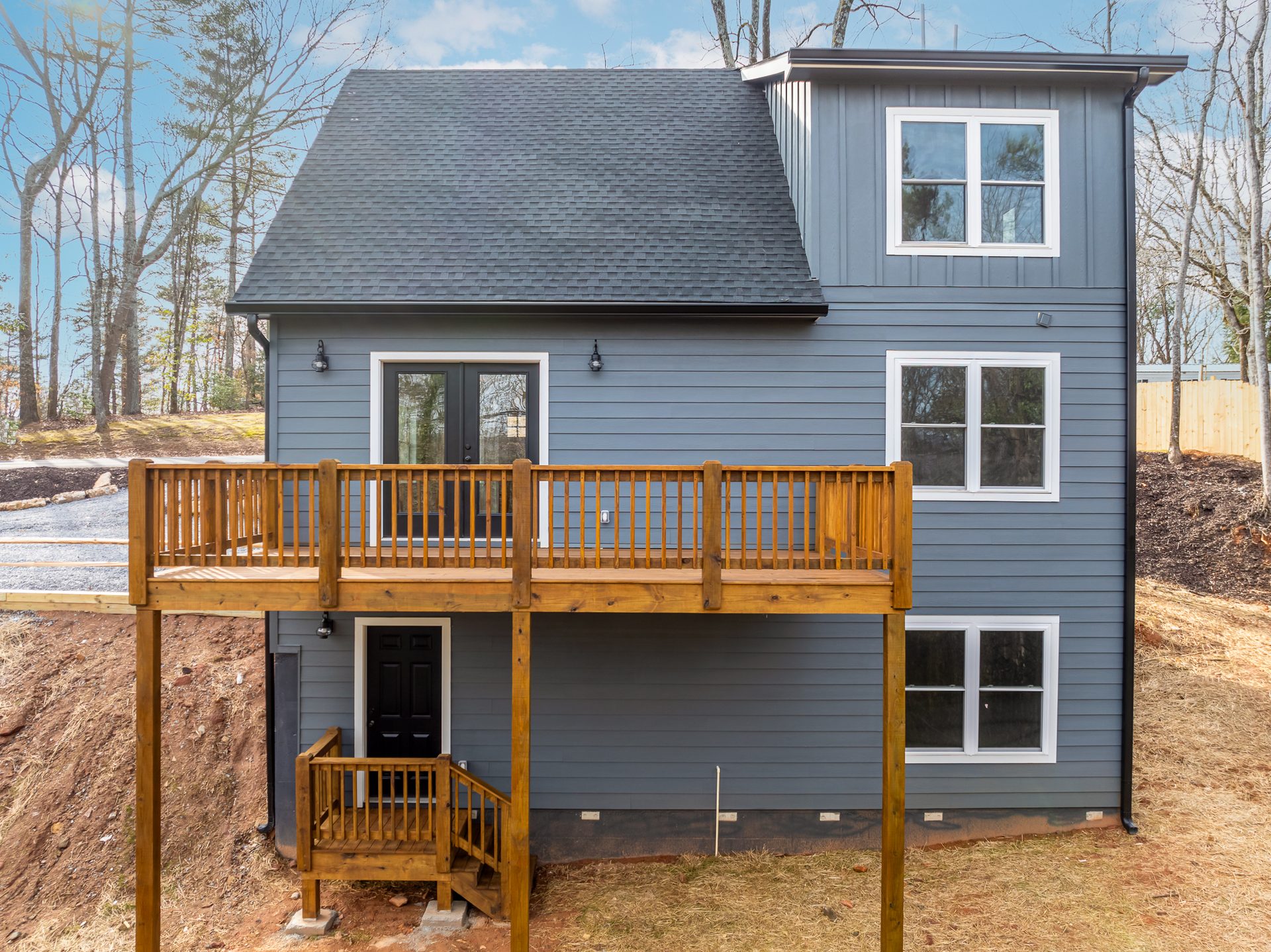 Rear of a blue-gray home on a slope with an elevated wood deck