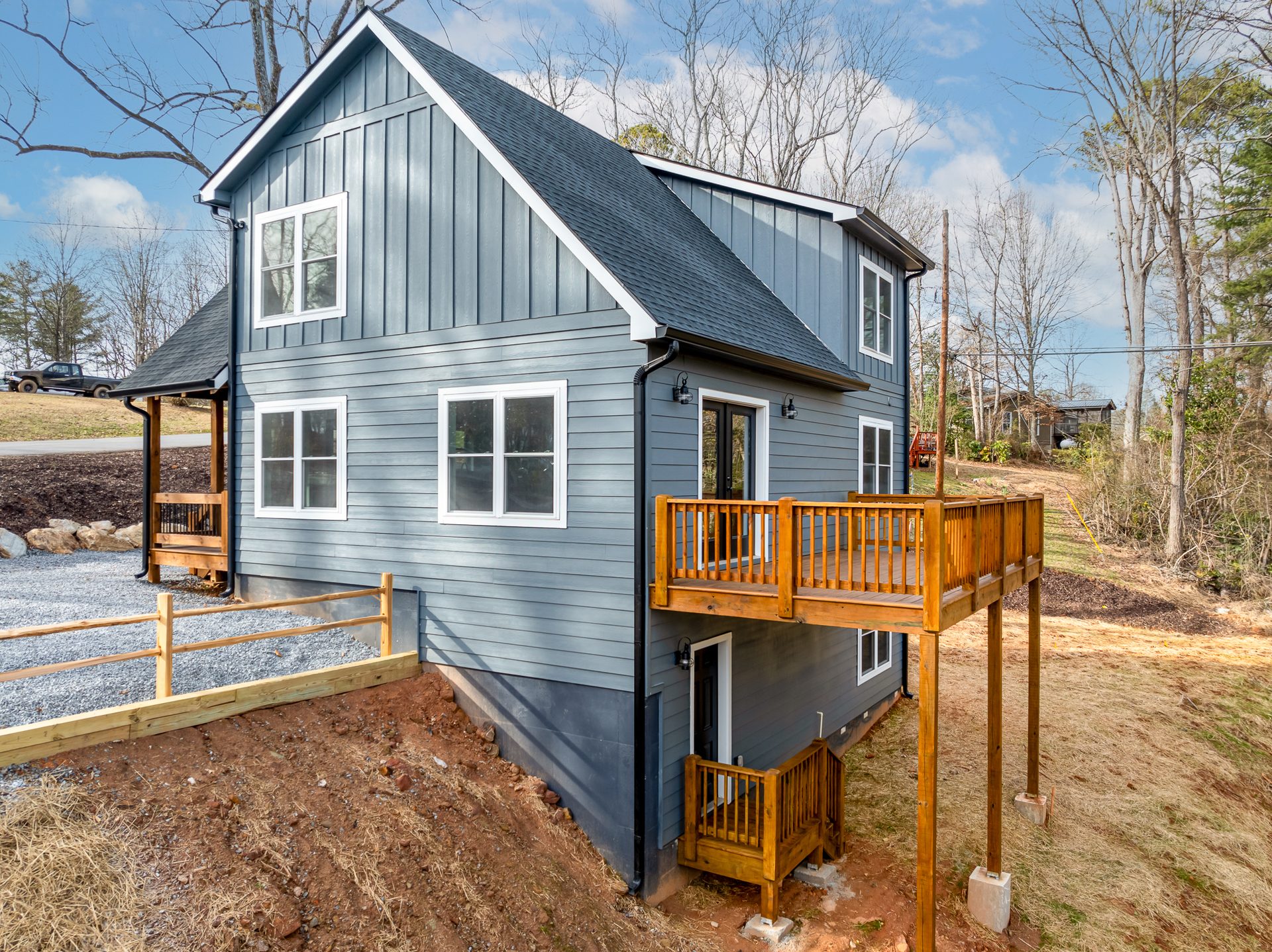 Rear three-quarter view of a blue-gray home and elevated deck beside a wood fence