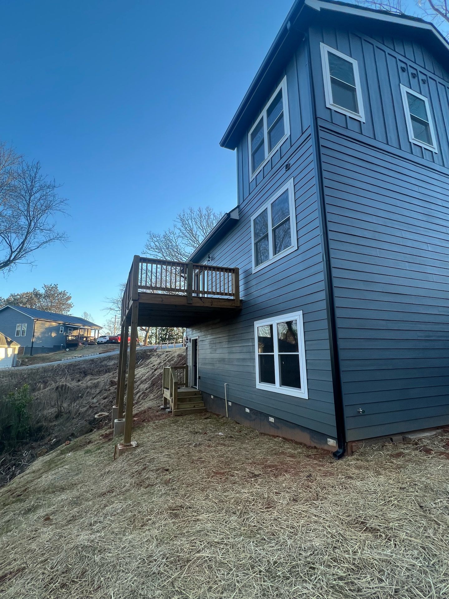 Low-angle view of a blue-gray home showing tall wood deck supports