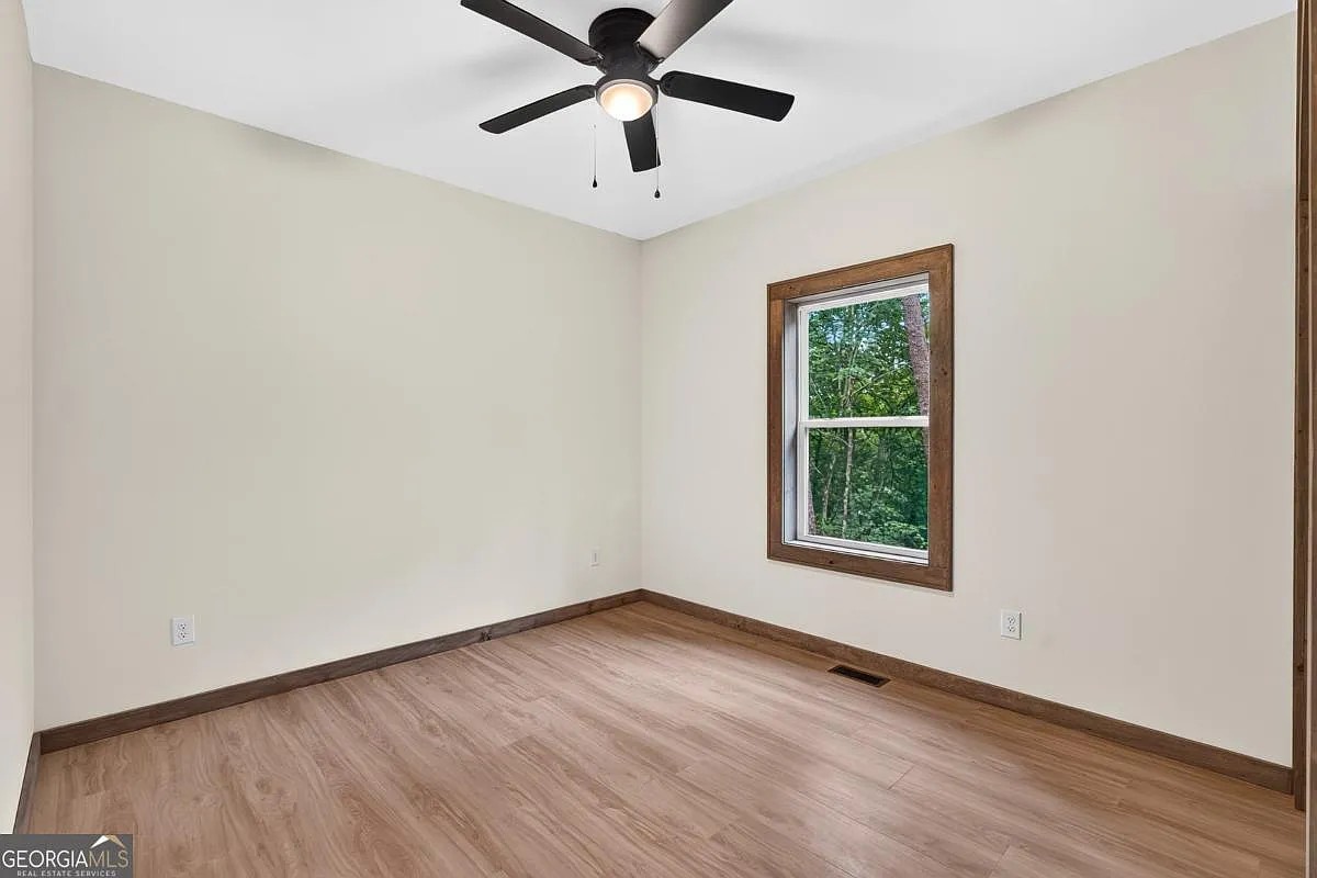 Bedroom with light wood floors, dark wood trim, a black ceiling fan, and a wooded-view window