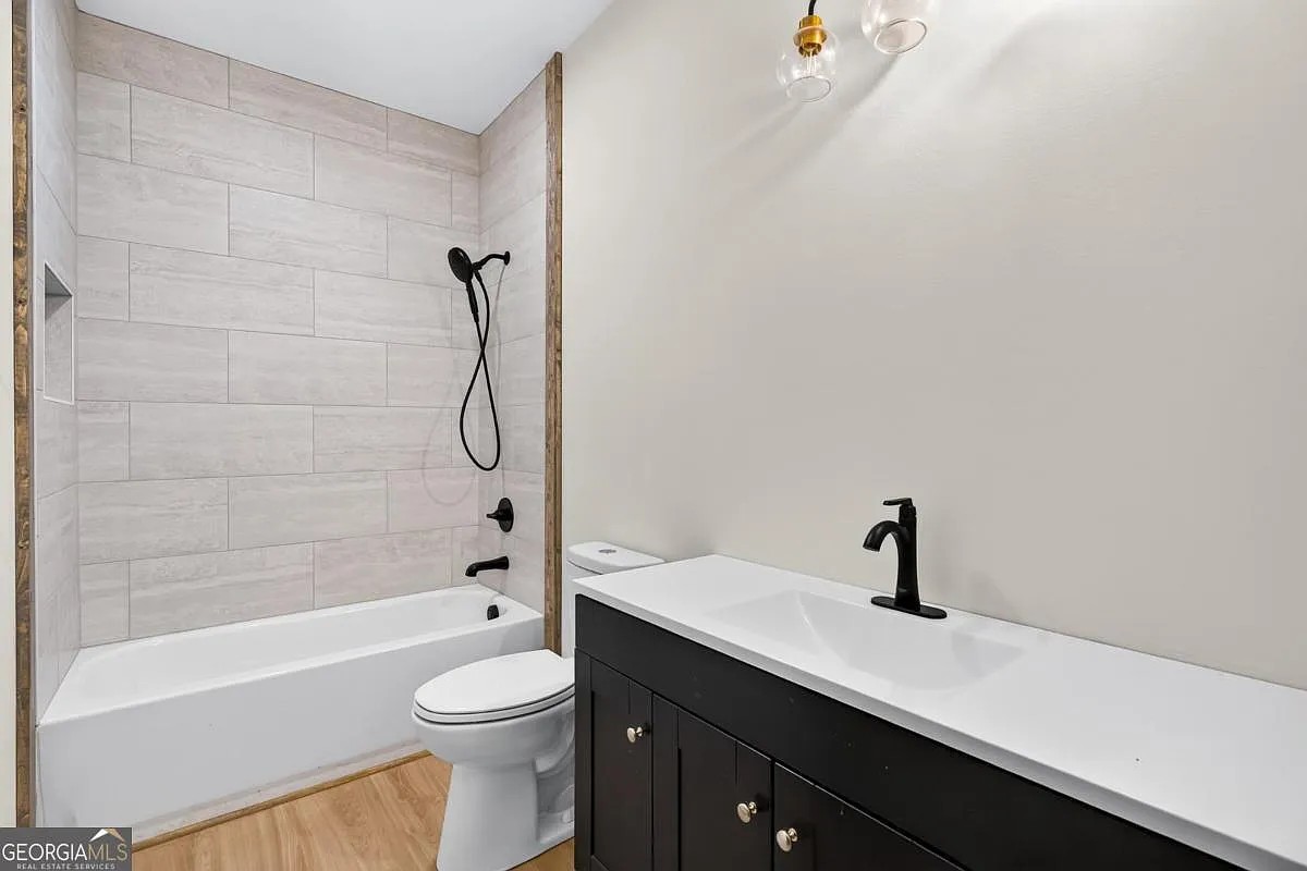 Bath with a tiled tub surround, dark vanity, and matte black fixtures