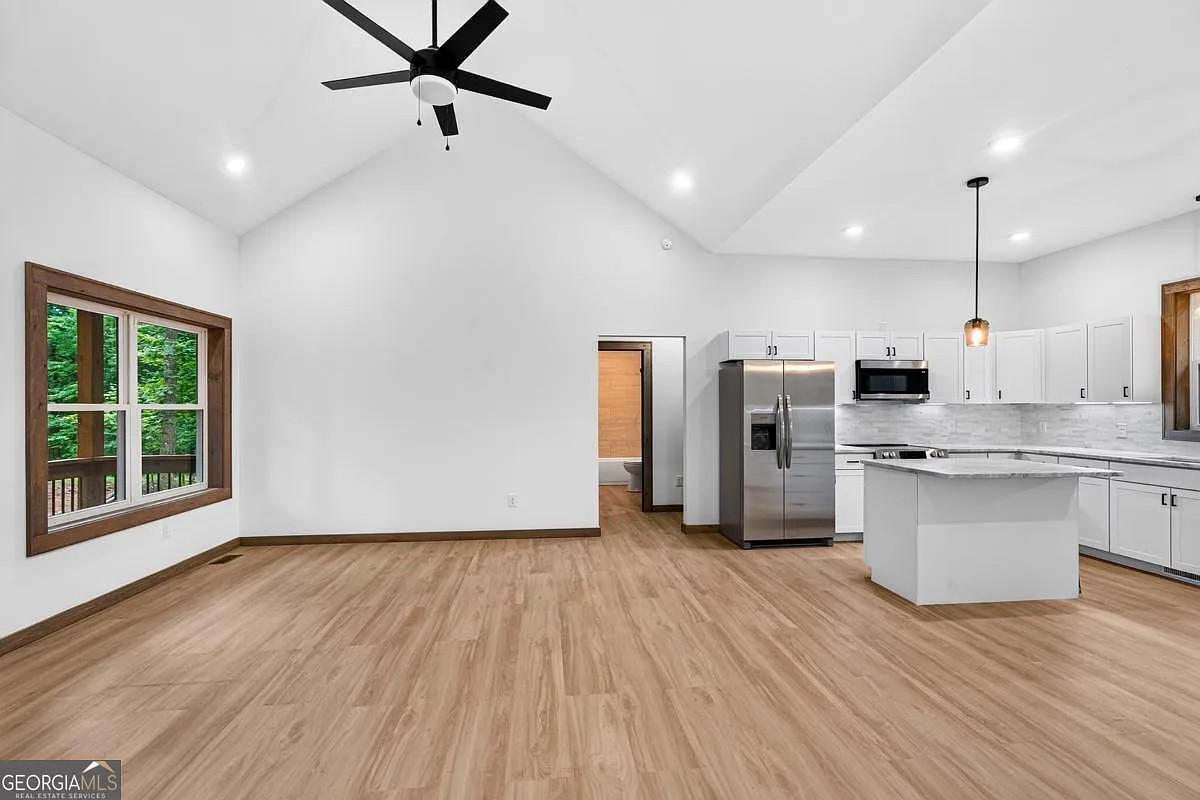 Open living area and kitchen with vaulted ceiling, white cabinets, and a window to the woods