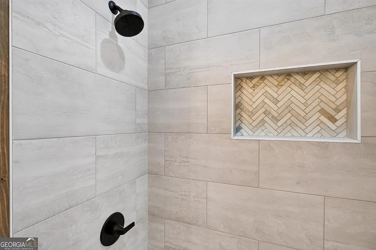 Walk-in shower with marble-look tile, matte black fixtures, and a herringbone niche