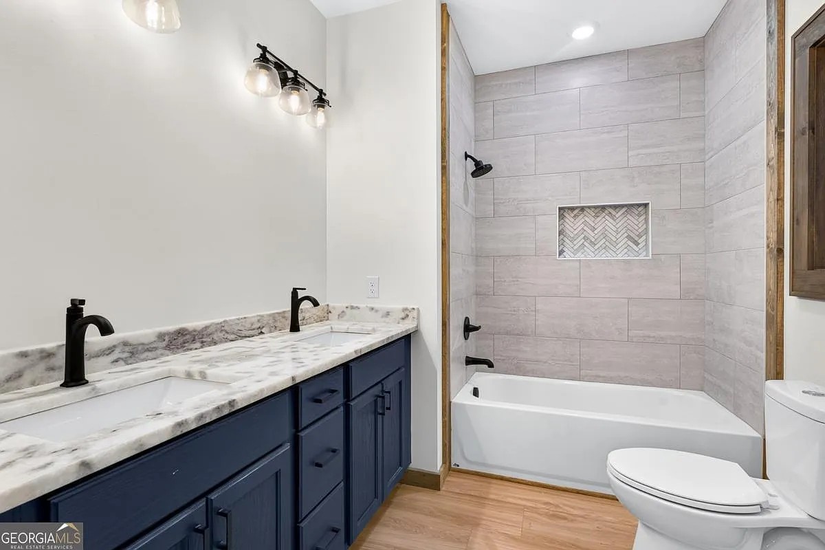 Bath with a navy double vanity, tiled tub surround, and matte black fixtures