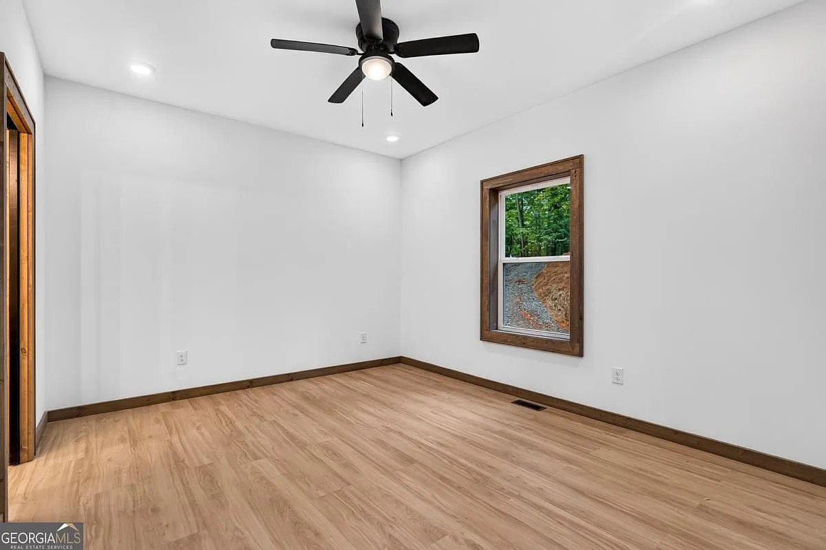 Bedroom with light wood floors, dark wood trim, a black ceiling fan, and a wooded-view window