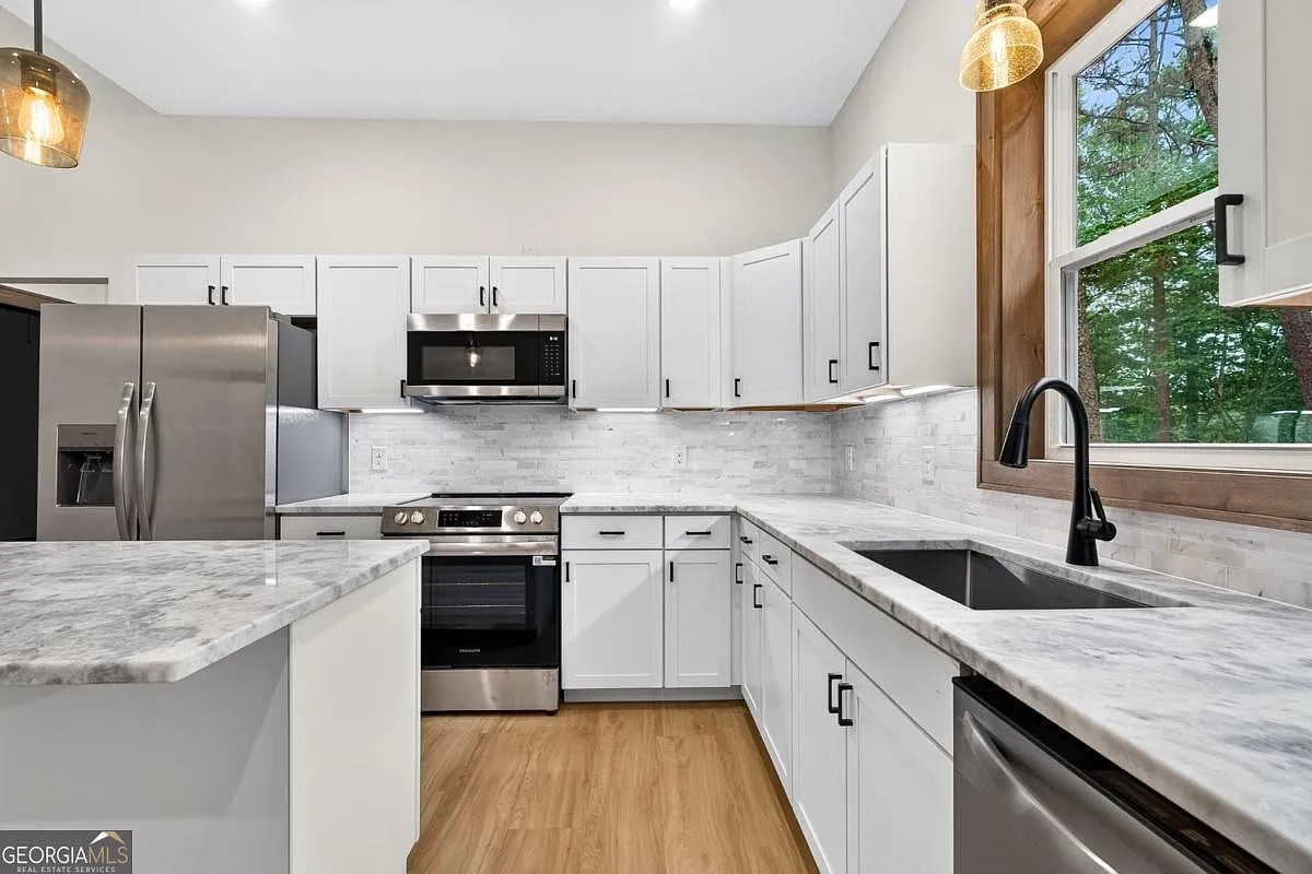 Kitchen with white cabinets, stainless appliances, and a wood-framed window over the sink