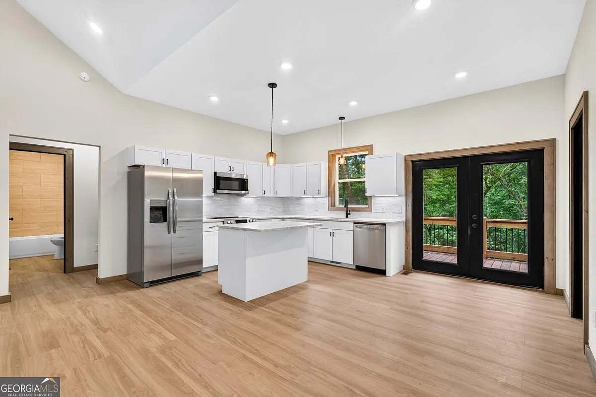 Open kitchen and living area with white cabinets and glass doors to a wood deck