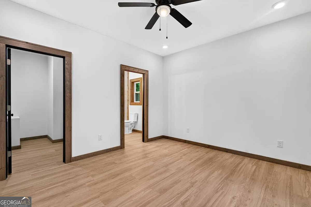 Bedroom with wood floors, dark wood trim, a ceiling fan, and an ensuite bath