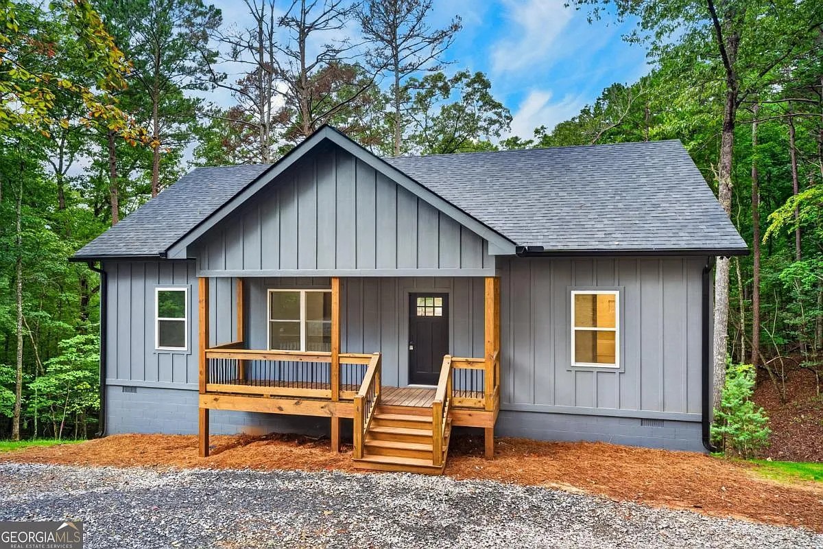 Front exterior of a dark gray home with a wood porch among the trees