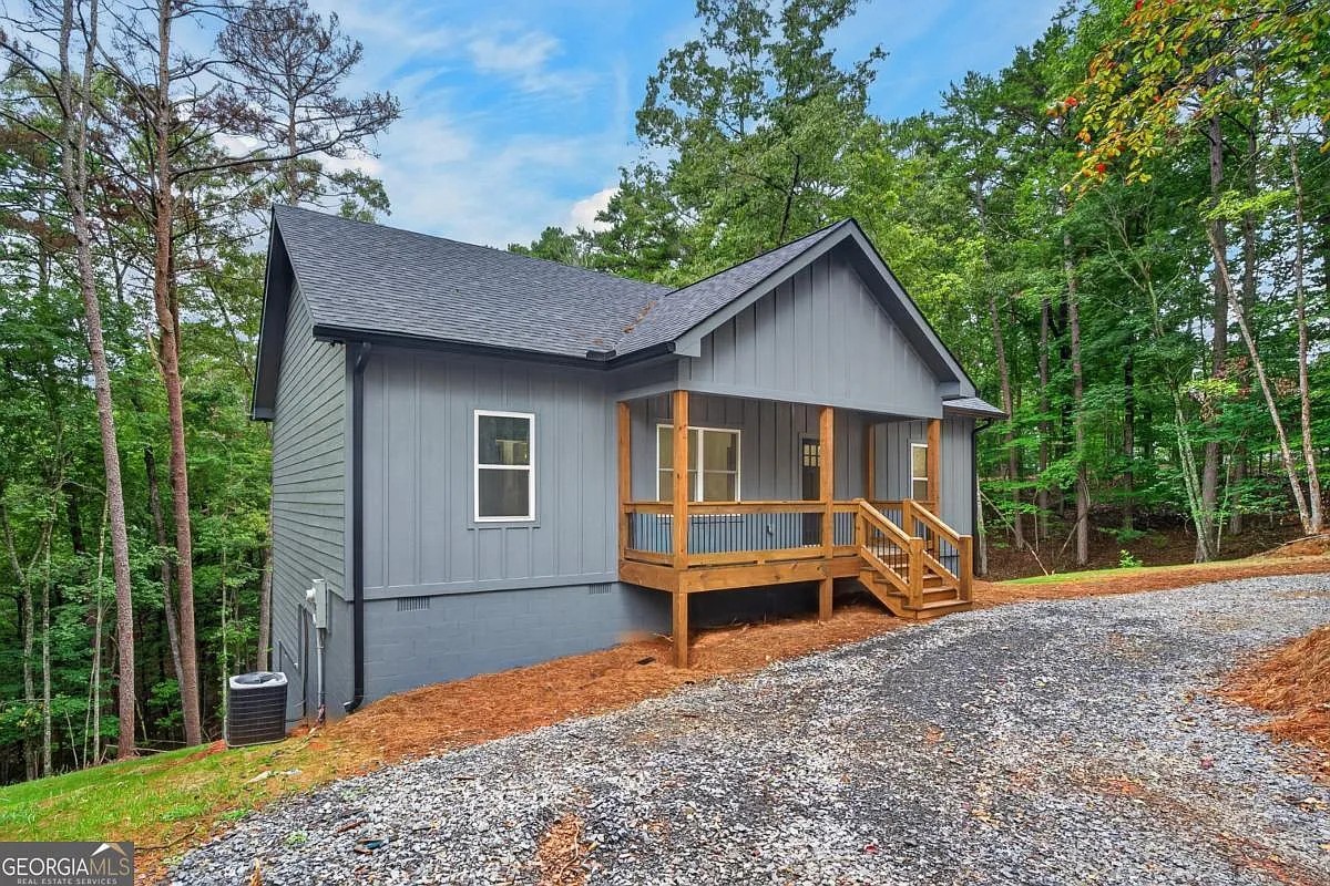 Side-front of a dark gray home with a wood porch and gravel driveway